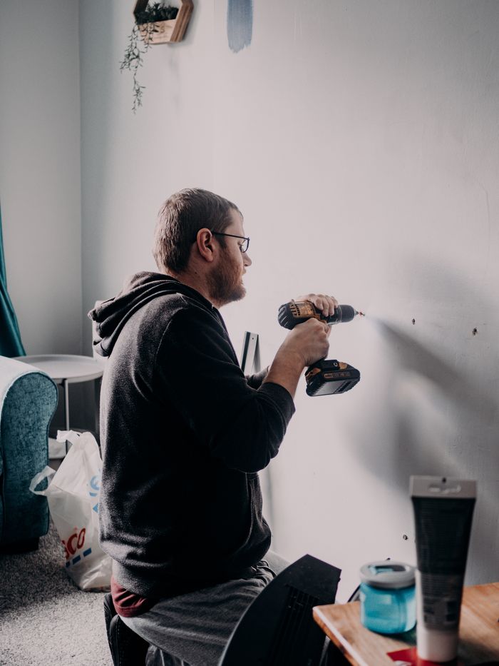 Adult man using a power drill indoors for home improvement in a well-lit room.